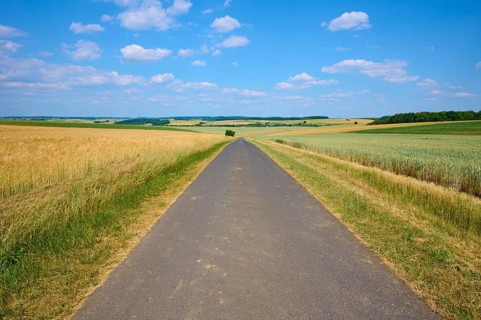 Straight road through wide fields under a blue sky with clouds, summer, Thüngen, Main Spessart