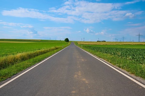 A straight country road between green fields under a blue sky with white clouds, Marktheidenfeld,