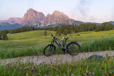 A bicycle stands on a gravel road with a view of the nearby Dolomites, Sassolungo Group, Alpe di