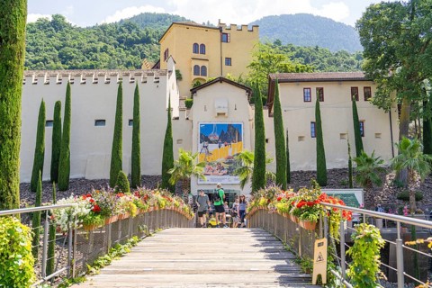 A bridge with flowers leads to colourful buildings in front of a mountainous landscape, Botanical
