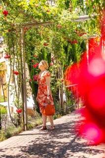 Woman in a red dress walks through a flowering garden pavilion, surrounded by green foliage,