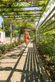 Woman in a pavilion, covered by leaves, with long shadows on the ground, surrounded by summer