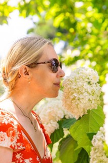 Woman smelling a white flower, surrounded by green plants, wearing a red dress, Botanical Garden,