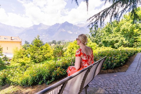 Woman in a red dress sitting on a bench with a view of mountains and nature, Botanical Garden, The