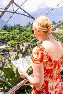 Woman in a red dress looking at a map near a structural glass construction, Botanical Gardens, The
