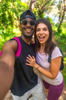 Happy couple taking a selfie while hiking on a forest trail, enjoying the beautiful nature