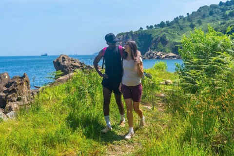 Interracial couple walking along a coastal path, enjoying the scenic views of the ocean and green