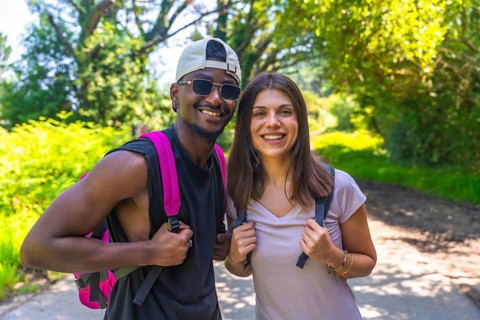Hikers wearing backpacks are smiling joyfully while trekking along a forest path, enjoying the