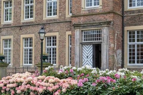 Brick building with large entrance door, blooming rhododendrons and an old lantern in the