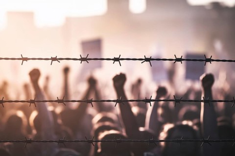 Barbed wire barrier with blurred protest crowd. A poignant image of resistance and struggle at