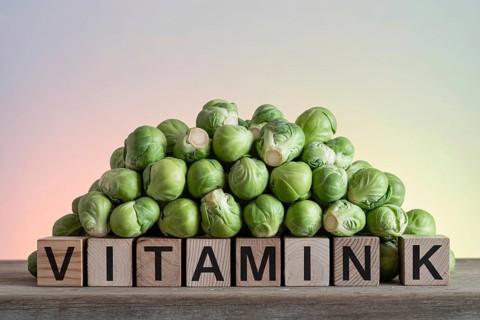 Brussels sprouts stacked on wood with blocks spelling Vitamin K. Rustic studio scene highlighting