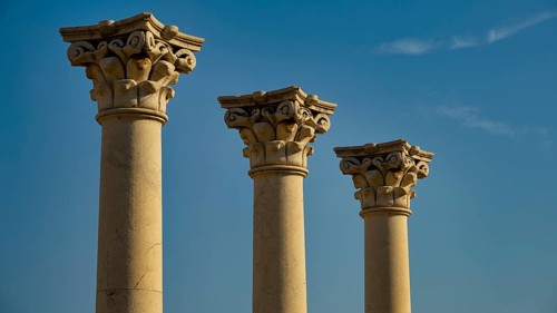 Three ornate ancient columns rising against the blue sky, Temple of Apollo, Corinthian Columns,