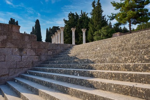Stone staircase with old columns, framed by trees under a blue sky, open staircase to the second