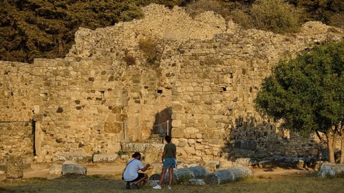 Two people in front of an old stone wall in a setting surrounded by trees, Roman bathhouse,