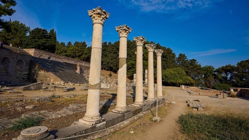 Row of ancient columns rises in a historic site surrounded by trees, Temple of Apollo, Corinthian