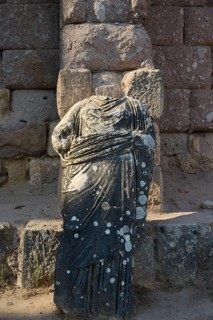 Damaged stone statue in antique garment in front of an old stone wall, antique statue of gods,