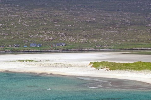 Tranquil coastal landscape with white sand and green land in flat light under a cloudy sky,