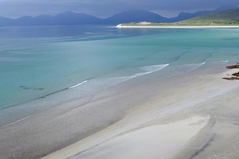 Gentle waves lap the wide, empty beach against a backdrop of mountains and a calm sea, Seilebost