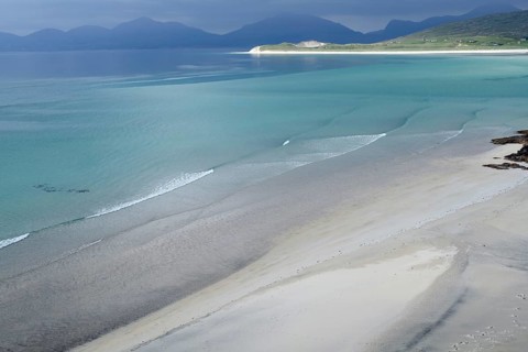 Gentle waves roll over fine sand against a majestic backdrop of mountains and calm sea, Seilebost