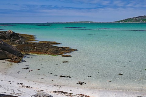 Tranquil beach landscape with rocks, sea and clear blue sky with seaweed on the shore, Eriksay,