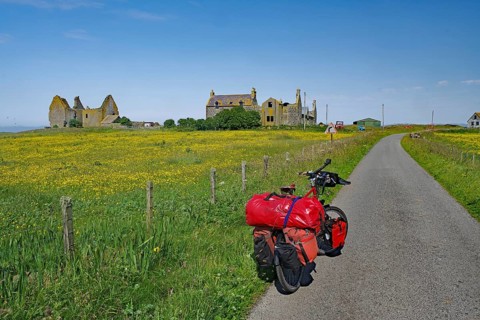 Luggage-laden bike on road next to flowering fields and ruins under clear sky, cycle tour, South
