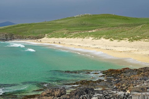 Picturesque coastal landscape with green hill, sandy beach and turquoise sea under a cloudy sky,