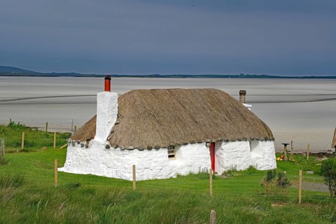 White thatched house on a green meadow against a sandy coastal background under a blue sky,