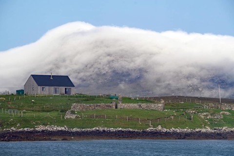 House on green meadow with sheep in front of misty hills on the coast, Benbecula, Hebrides,
