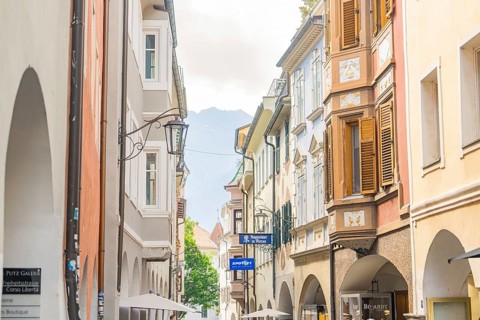 Narrow alley in the old town centre with classic buildings and shutters, mountains in the