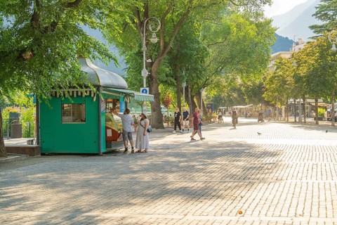 People walking on a sunny promenade with an ice cream shop in the foreground, Merano, Italy