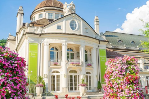A magnificent baroque building with flowerbeds and flowering plants in the foreground, Merano,