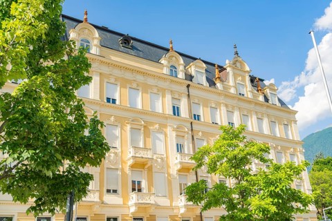 Classic building with elegant façade flanked by green trees under a blue sky on a sunny day,