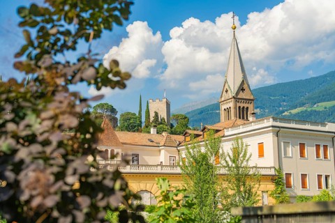 Historic building with church tower and picturesque mountains in the background under a cloudy sky,