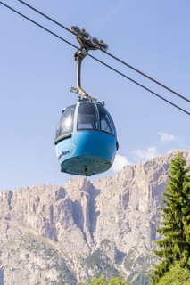 Blue cable car gondola floating in front of an impressive mountain range under a clear sky, Alpe di
