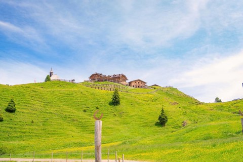 Wooden building on a green hill in front of a blue sky with white clouds, Alpe di Siusi, Dolomites,