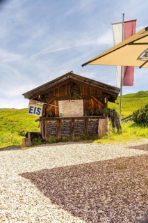 Wooden hut as an ice cream stand in a meadow in the mountains in the sunshine with flags and