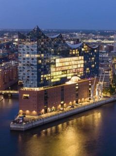 Aerial view of the Elbphilharmonie at blue hour with illuminated windows and view over the