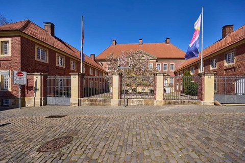 Cathedral administration, brick building, tree, cobblestone pavement, flags on flagpoles, blue