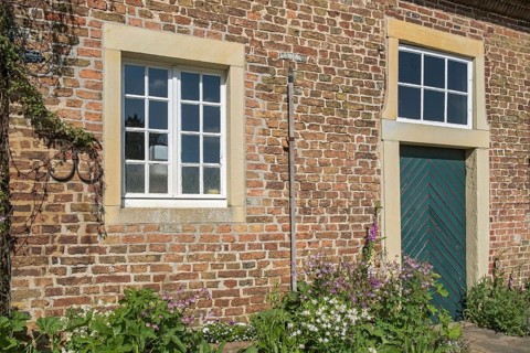 A rustic brick wall with two windows, wooden door and flowering plants, Haus Welbergen, Ochtrup,