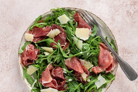 Fresh arugula salad with prosciutto and grated parmesan cheese, on a plate, homemade, no people