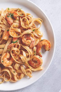 Fettuccine pasta with shrimp, spicy in soy sauce, on a grey plate with a fork, close-up