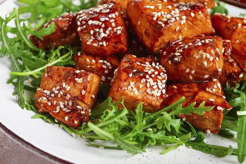Fried salmon slices, teriyaki with sesame seeds, with arugula salad, top view