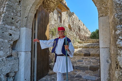 Man in traditional traditional costume kindly standing in front of historic archway, Antimacheia,