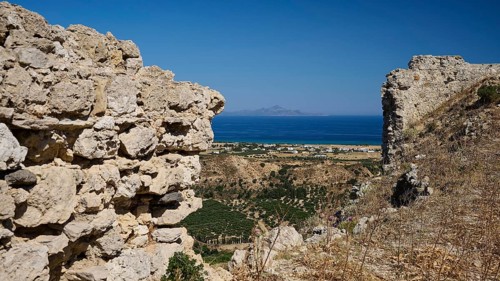 View through ancient ruins to a rocky landscape with the sea in the background, Kardamina,