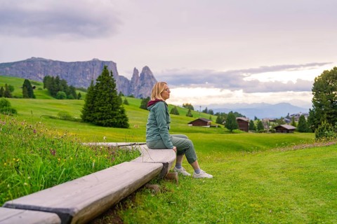 Woman enjoying the view in a green hilly landscape with mountains and clouds, Alpe di Siusi, South