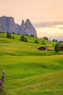 Green hills at sunset with wooden huts and mountains in the background, Alpe di Siusi, South Tyrol,