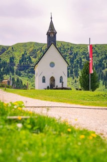 White church stands idyllically on a green meadow with mountain backdrop and flag, Alpe di Siusi,