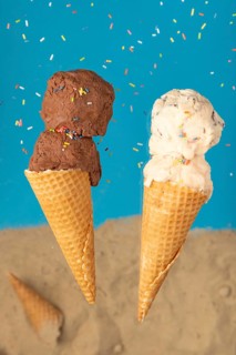 Two ice cream cones, one with chocolate ice cream and one with cream ice cream, against a blue