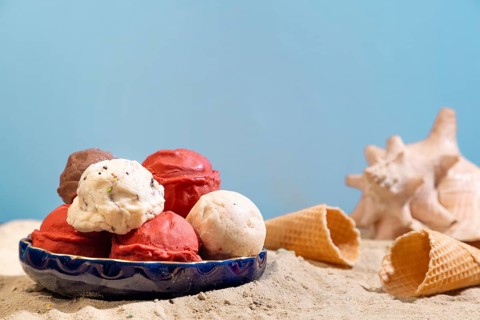 Different flavours of ice cream on a plate on the beach, with blue background and shell