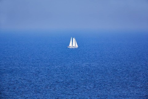 Blue sea, calm water surface, single sailing boat on the horizon, haze, offshore island Helgoland,